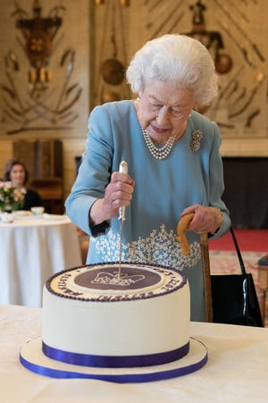 Queen Elizabeth II cuts a cake with a Platinum Jubilee emblem during a reception for local residents and charities at Sandringham House in Norfolk, on Feb. 5, 2022.