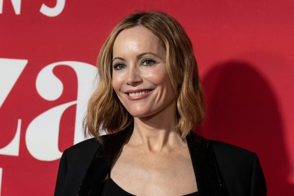 Leslie Mann wears a black jacket on the red carpet against a red backdrop