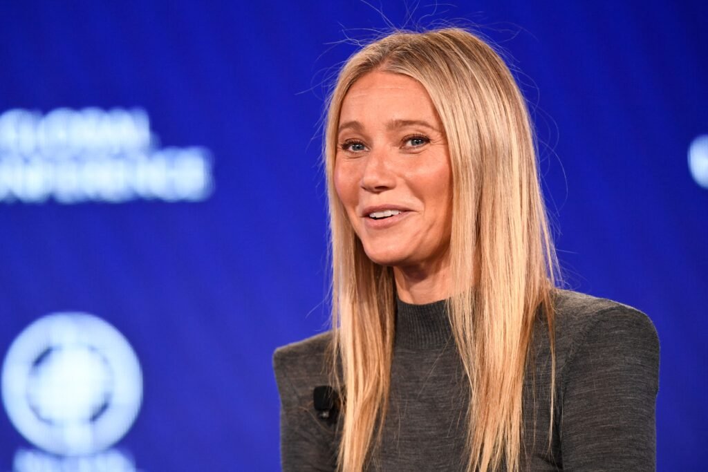Gwyneth Paltrow smiling in gray sweater against blue backdrop