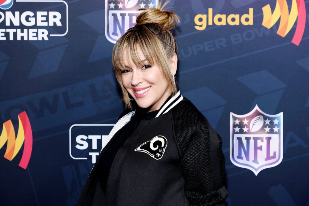 Alyssa Milano smiling in black and white track jacket against navy blue backdrop