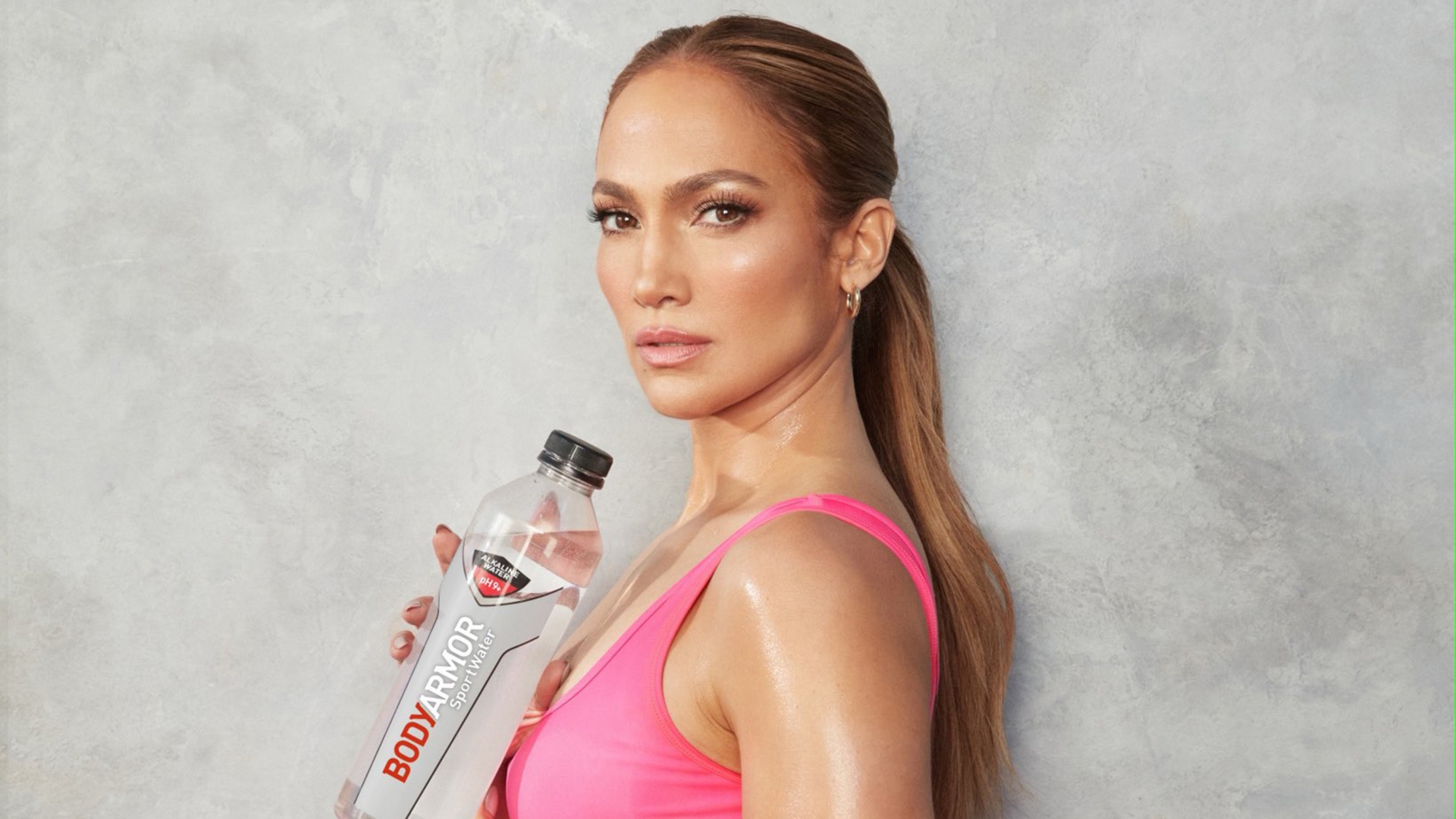 Jennifer Lopez, 53 years old, is a famous figure sporting pink cycling shorts and a sports bra to promote sports drinks