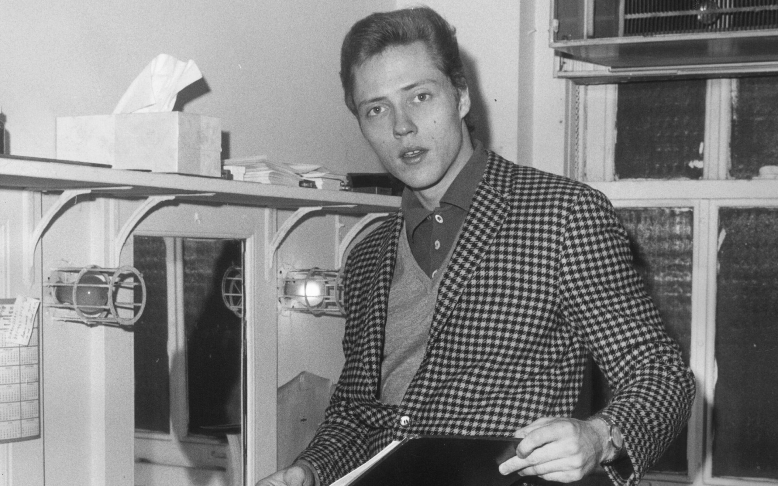 circa 1965:  American actor Christopher Walken resting his foot on a chair while examining a script in a dressing room.  Walken wears a checkered jacket. 